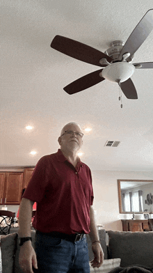 a man in a red shirt stands in front of a ceiling fan in a living room