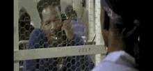 a man is talking on a cell phone in a prison cell .