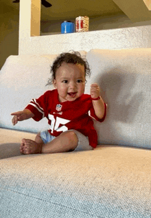 a baby is sitting on a couch wearing a red jersey with the number 12 on it