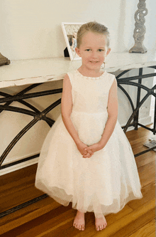 a little girl in a white dress stands in front of a picture frame