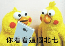 two stuffed yellow birds are looking at a cell phone .