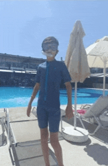 a boy wearing a mask and goggles is standing next to a swimming pool .