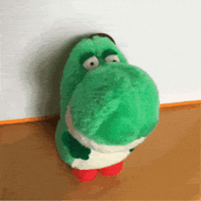 a green stuffed animal with big eyes is sitting on a wooden surface