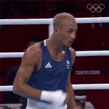 a man in a blue tank top is standing in a boxing ring with his hands in his pockets .