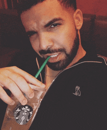 a man with a beard is drinking from a starbucks cup with a green straw