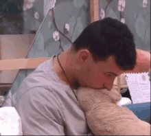 a man is sitting on a bed with his head on a pillow and a teddy bear .