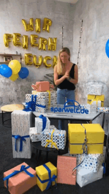 a woman stands in front of a table full of gifts and balloons with wir feiern euch written on it