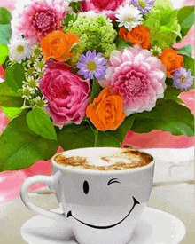 a cup of coffee with a smiley face and a bouquet of flowers in the background