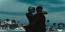 a man and a woman are hugging each other in front of a city at night