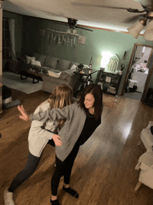 two girls are dancing in a living room with a ceiling fan and a sign that says ' i love you ' on it