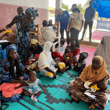 a group of people are sitting on a mat with a man wearing a blue shirt that says unicef