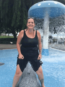 a woman in a black tank top stands in front of a fountain