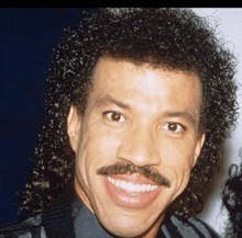 a man with curly hair and a mustache is smiling for the camera