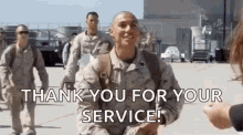 a group of soldiers are walking down a runway and a woman is giving them a thank you for their service sign .