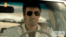 a man wearing sunglasses is driving a car with a giflab logo in the background