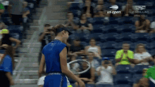 a woman in a blue shirt is holding a tennis racquet in front of a crowd sponsored by us open