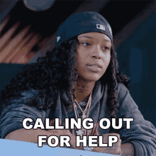 a woman with curly hair is sitting at a table with the words " calling out for help " above her