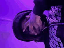 a person covering their face with their hands in front of a purple light