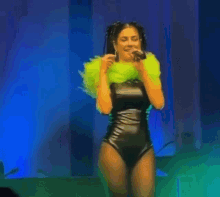 a woman is singing into a microphone while wearing a black bodysuit and a green feathered collar