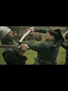 two men are fighting with swords in a field and one is wearing a hat