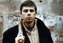 a man in a sweater holds a gun in front of a wall