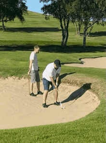 two men are playing golf on a golf course and one of them is hitting a ball out of a bunker