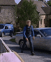 a man standing next to a silver car with a van in the background that says ' a & a ' on it