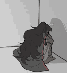 a person with long black hair is sitting in a corner of a room .