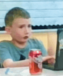 a boy is sitting at a table with a can of soda and a laptop .