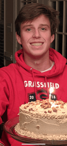 a young man wearing a grassfield sweatshirt holds a cake