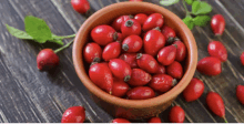 a bowl filled with red berries is on a wooden table