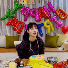 a woman is sitting at a table with a cake and balloons behind her that say ' happy birthday '