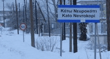 a blue sign is sitting in the snow in front of a snow covered forest .