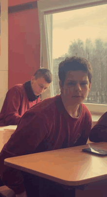 a boy in a red shirt is sitting at a desk