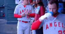 a group of baseball players are standing in a dugout and one of them is drinking from a cup .