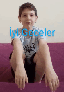 a boy wearing a shirt that says iyi geceler is sitting on a couch