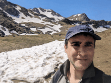 a man wearing a hat stands in front of a snowy mountain