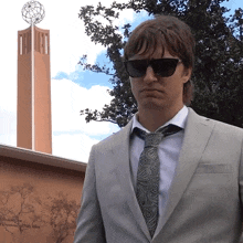 a man wearing sunglasses and a suit stands in front of a building that says " international public affairs "