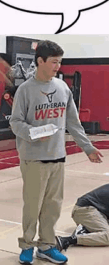 a young man wearing a lutheran west shirt is standing on a basketball court .