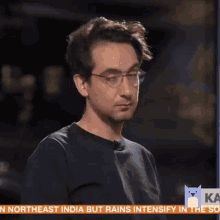 a man wearing glasses stands in front of a screen that says " northeast india but rains intensify in the so "