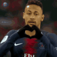 a man in a fly emirates jersey is making a heart shape with his hands .