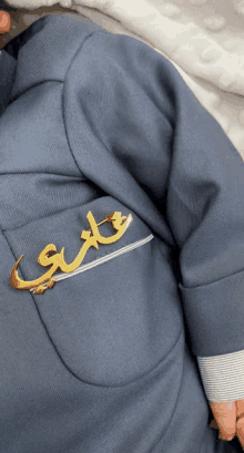 a baby wearing a blue jacket with a gold brooch that says " علي "