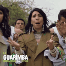 a woman in a trench coat stands in front of a group of people at the guarimba international film festival