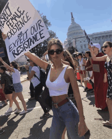 a woman holds up a sign that says expect female existence or expect our resistance