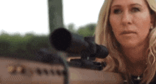 a woman is holding a rifle with a scope on it and looking through it .