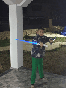 a young boy in green pants holds a light saber