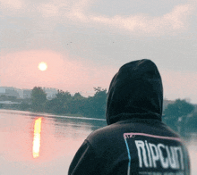 a person wearing a black ripcurl hoodie looks at the sunset