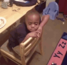 a young boy is sitting in a wooden chair with his head resting on the back of the chair .