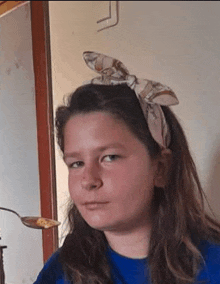 a young girl wearing a headband and a blue shirt is holding a spoon .