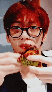 a young man wearing glasses is eating a hamburger